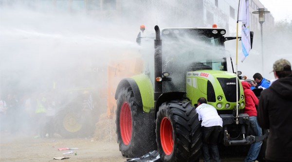 Protestors take cover behind a tractor from a water canon during a farmers demonstration in front of the European Commission building on September 7, 2015, in Brussels, as European agriculture ministers hold an extraordinary meeting at the European Council. Thousands of angry European farmers set off fireworks, blared horns and blocked Brussels streets with tractors as they demanded emergency European Union funds to help them cope with plunging food prices and soaring costs AFP PHOTO / EMMANUEL DUNAND